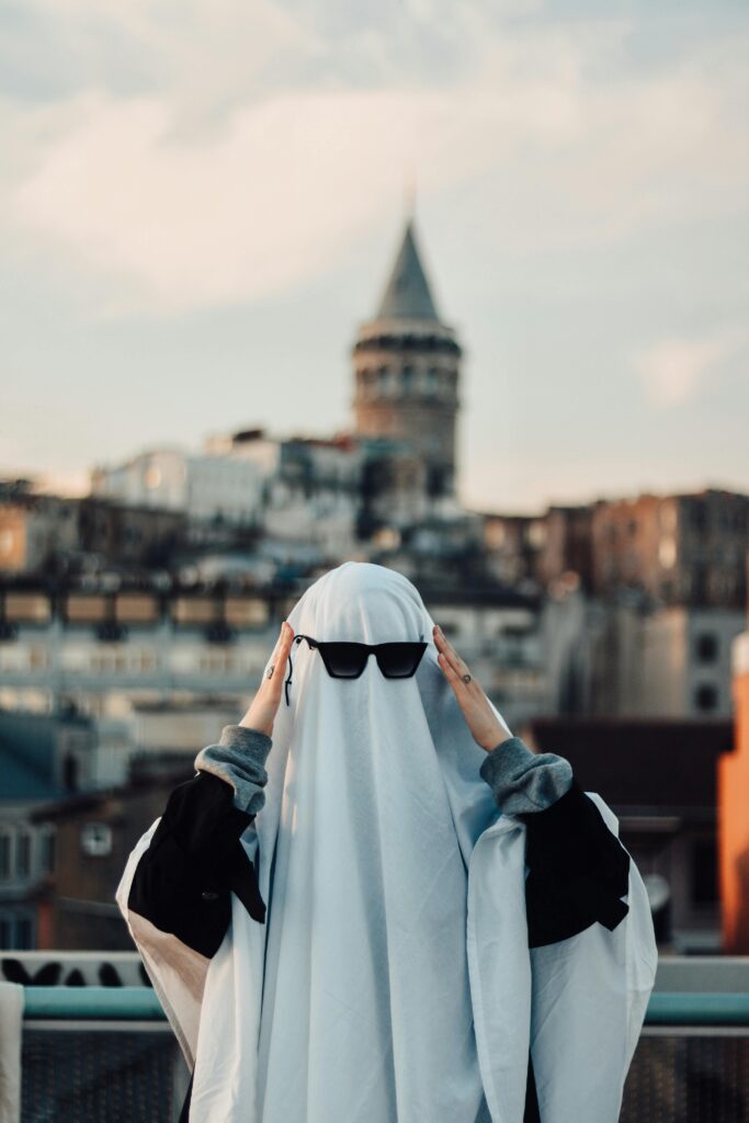 A whimsical Halloween ghost costume wearing sunglasses against an urban backdrop featuring a famous tower.